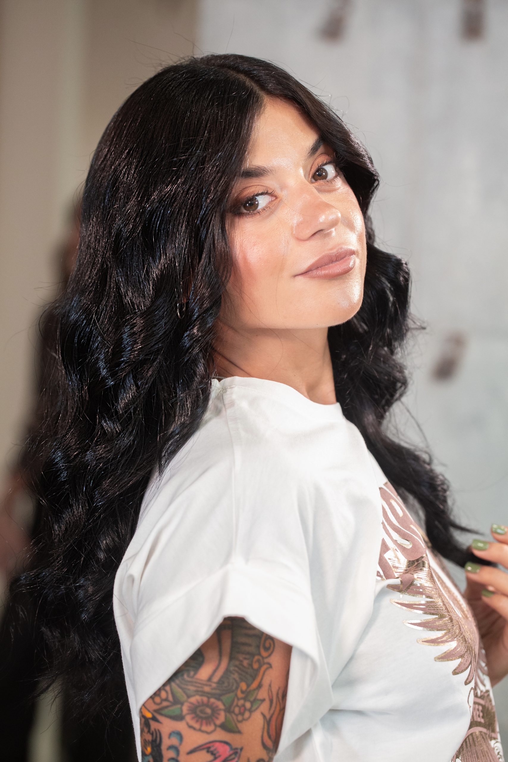 Mujer con cabello ondulado oscuro mirando a cámara, mostrando el resultado del peinado en el salón de belleza.