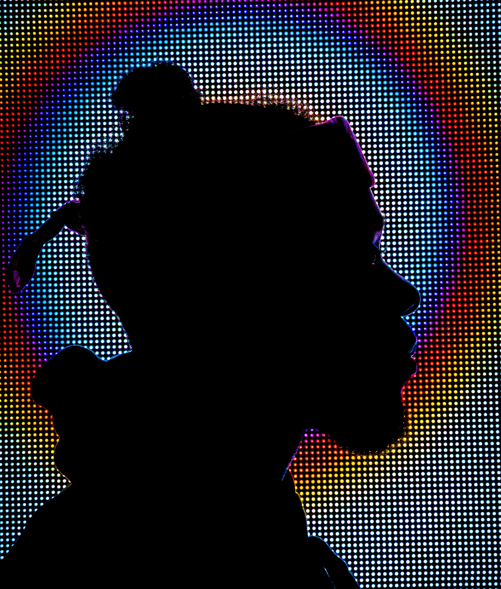Silueta de una persona de perfil frente a un fondo de luces LED multicolores, creando un contraste vibrante entre la figura oscura y el fondo brillante.