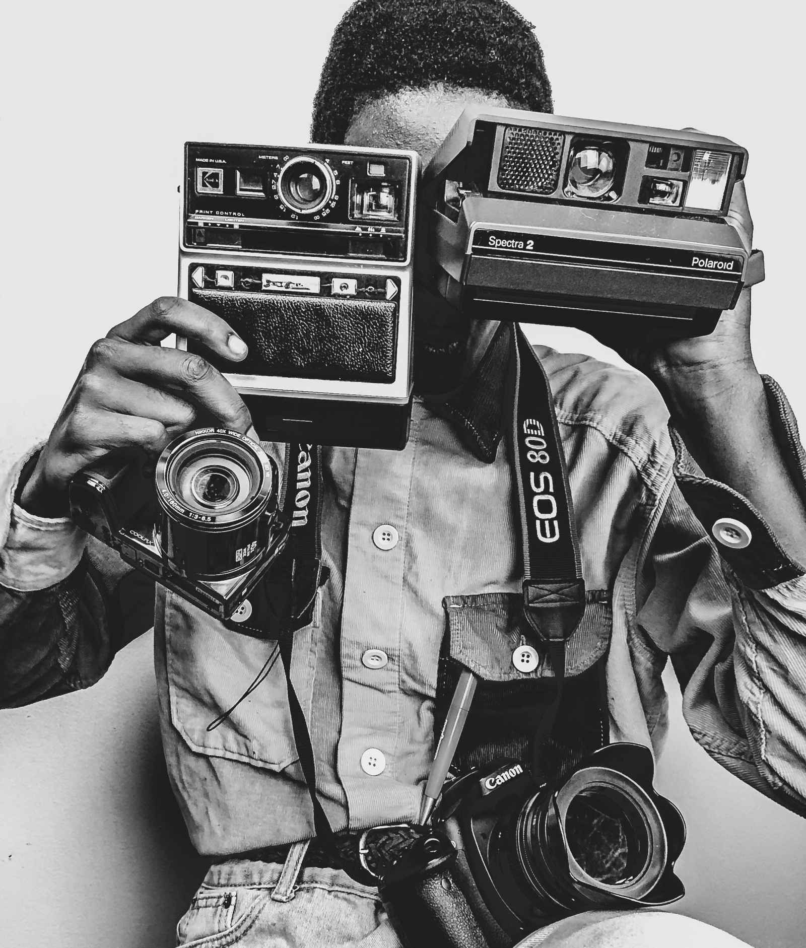 Persona sosteniendo dos cámaras Polaroid frente a su rostro mientras lleva colgadas varias cámaras Canon en blanco y negro, creando una composición visual centrada en la fotografía y la tecnología vintage.