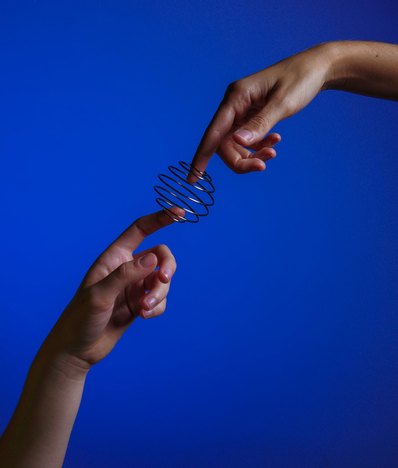 Dos manos sosteniendo un resorte metálico en medio de un fondo azul vibrante, creando una sensación de conexión y equilibrio.